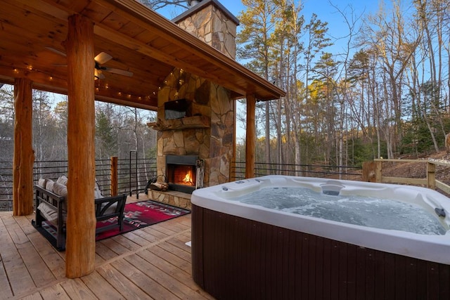 wooden terrace with ceiling fan, a hot tub, and an outdoor stone fireplace