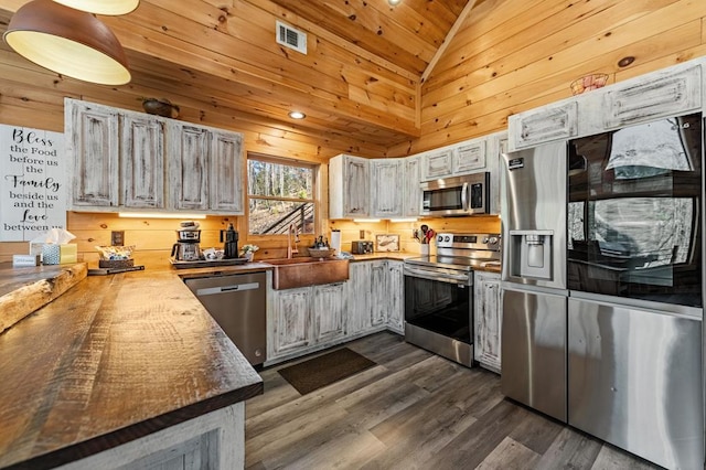 kitchen featuring wood walls, white cabinetry, sink, stainless steel appliances, and dark wood-type flooring