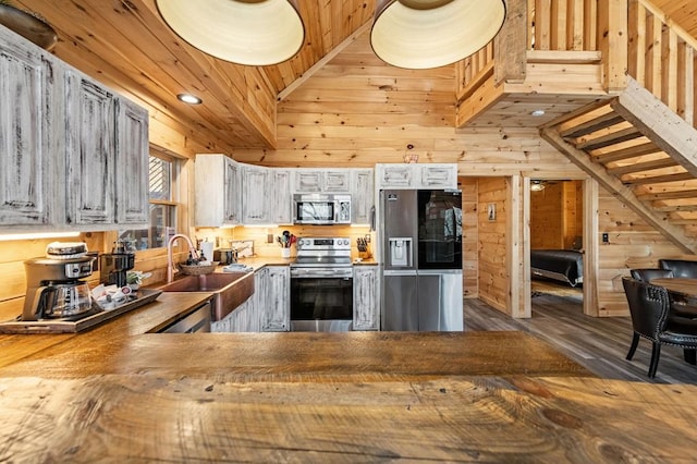 kitchen with hardwood / wood-style floors, wood walls, wood ceiling, kitchen peninsula, and stainless steel appliances