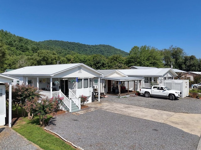 ranch-style house with gravel driveway, covered porch, metal roof, and a wooded view