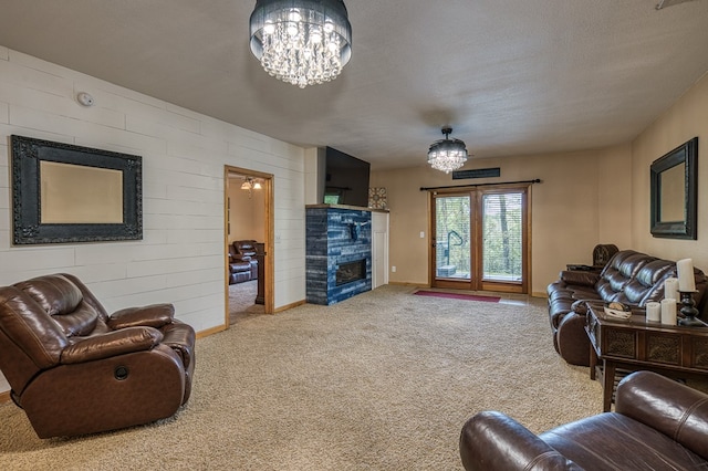 carpeted living room featuring wooden walls, an inviting chandelier, a fireplace, a textured ceiling, and baseboards