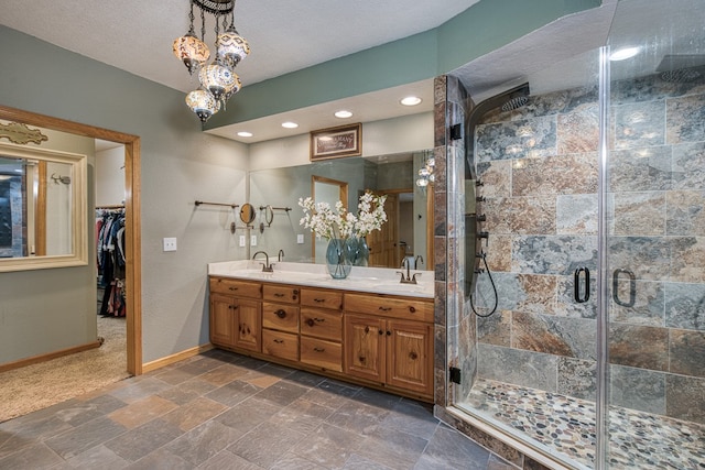 bathroom featuring double vanity, a stall shower, a sink, baseboards, and stone tile flooring
