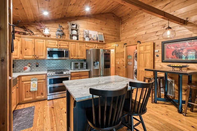 kitchen featuring wood ceiling, stacked washer / drying machine, stainless steel appliances, and wood walls
