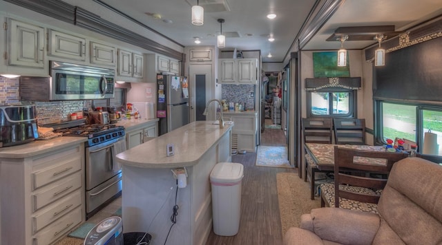 kitchen with hardwood / wood-style floors, an island with sink, decorative light fixtures, and stainless steel appliances