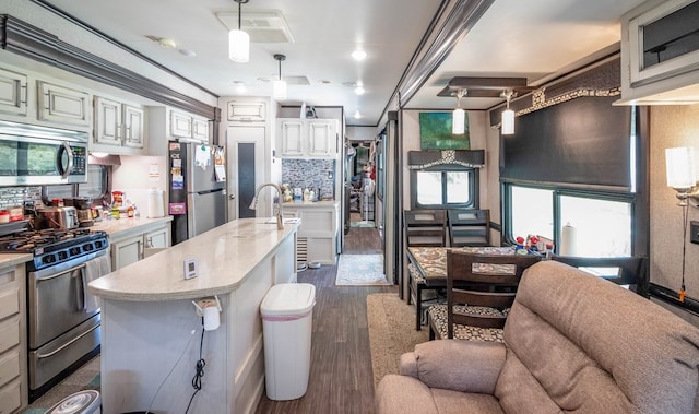 kitchen featuring a kitchen island with sink, hanging light fixtures, crown molding, appliances with stainless steel finishes, and dark hardwood / wood-style flooring