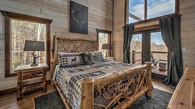 bedroom featuring hardwood / wood-style floors, wooden walls, access to exterior, french doors, and multiple windows