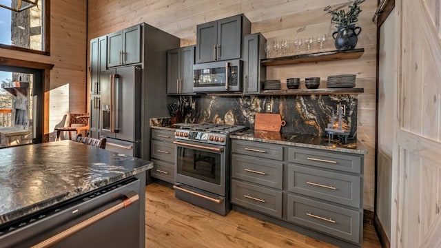 kitchen with high quality appliances, wooden walls, open shelves, light wood-type flooring, and dark stone countertops