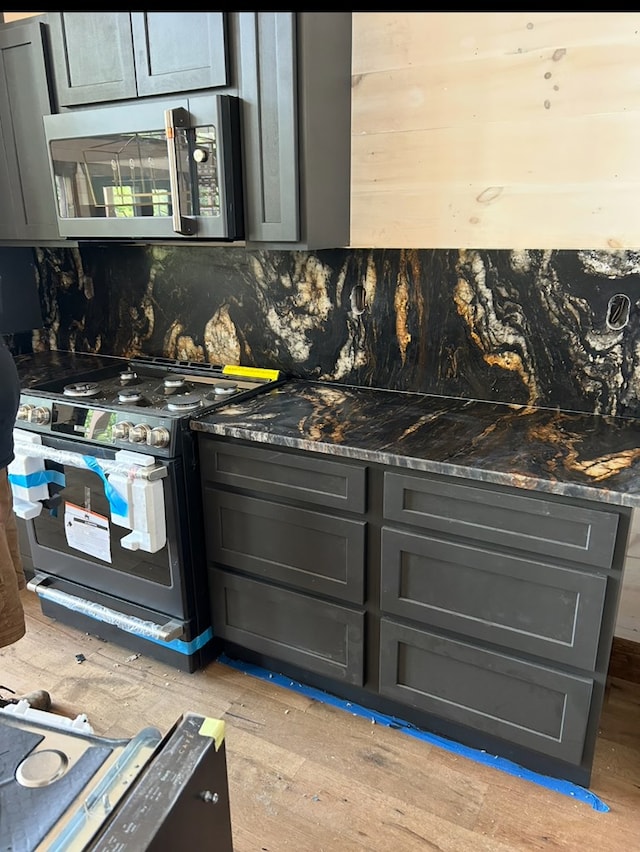 kitchen featuring stainless steel microwave, black electric range oven, tasteful backsplash, light wood finished floors, and dark stone countertops