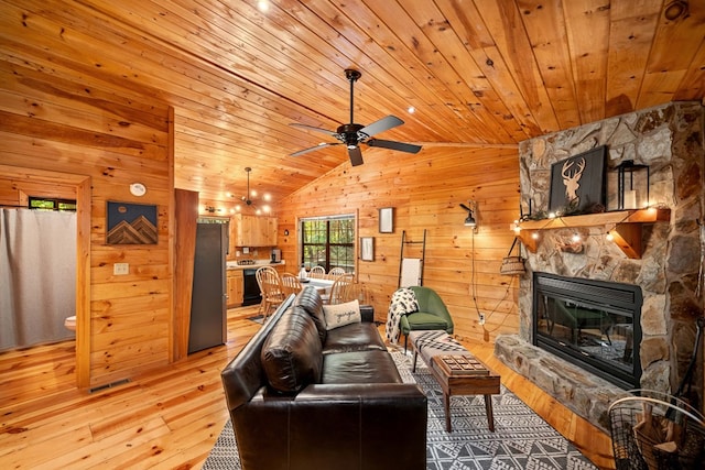 living room featuring a stone fireplace, wooden walls, vaulted ceiling, and light wood-type flooring