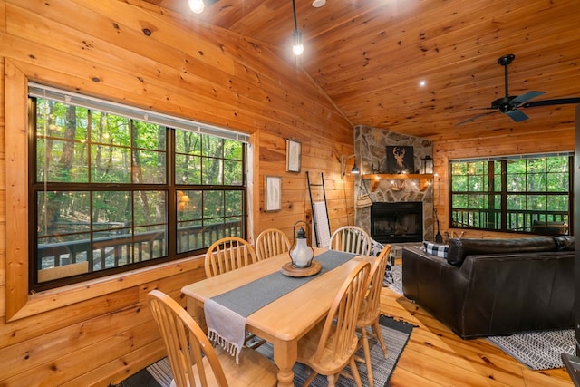 dining area with lofted ceiling, wood walls, wooden ceiling, a fireplace, and light hardwood / wood-style floors