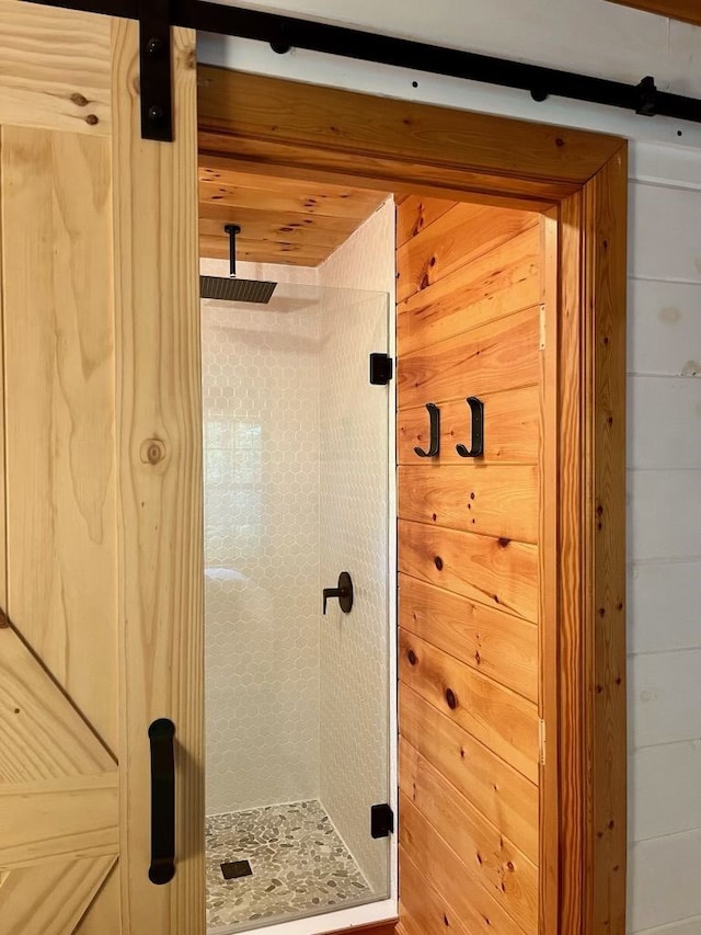 bathroom with a shower with shower door and wood walls