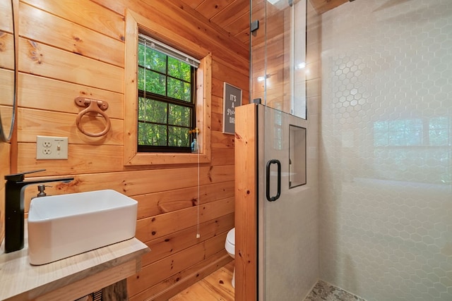 bathroom featuring toilet, a tile shower, sink, and wood walls