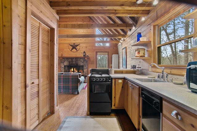 kitchen with a fireplace, wooden walls, sink, black appliances, and light hardwood / wood-style flooring