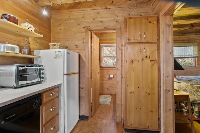 kitchen featuring wood walls, light wood-type flooring, white refrigerator, dishwasher, and a wealth of natural light