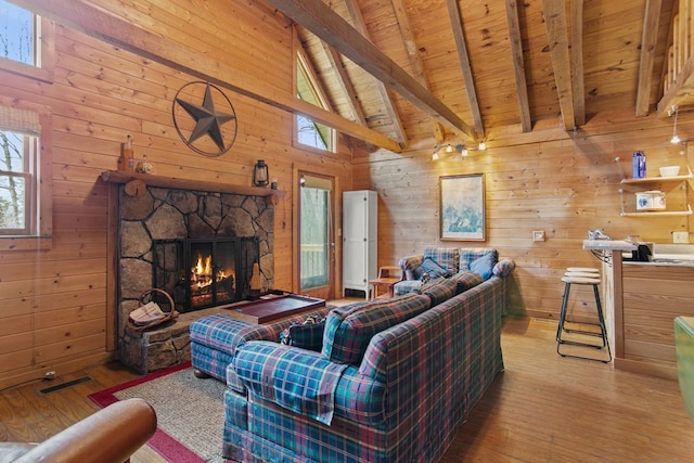 living room with light hardwood / wood-style flooring, beam ceiling, wooden walls, and a stone fireplace