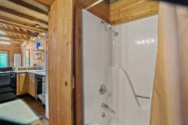 bathroom with wood-type flooring, beam ceiling, shower / tub combo, and wood walls