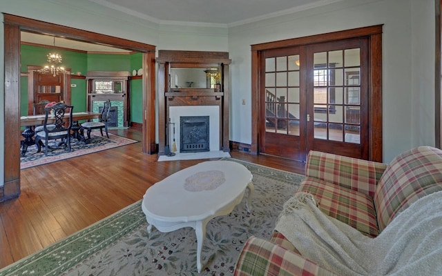 living room featuring a chandelier, a fireplace with flush hearth, crown molding, and wood finished floors