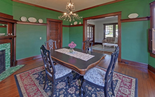 dining room featuring baseboards, ornamental molding, a chandelier, a fireplace, and wood-type flooring