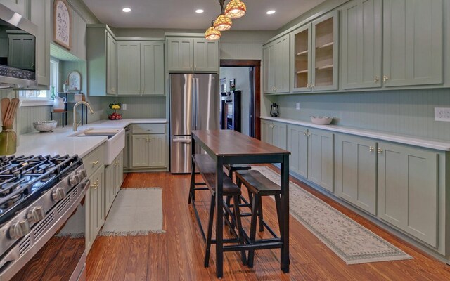 kitchen with appliances with stainless steel finishes, wood finished floors, light countertops, and green cabinetry