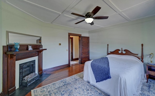 bedroom featuring a fireplace with flush hearth, a ceiling fan, wood finished floors, coffered ceiling, and baseboards