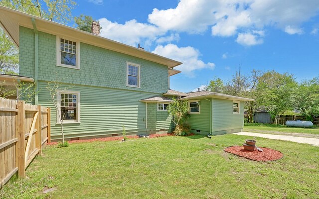 rear view of house featuring crawl space, a chimney, fence, and a lawn