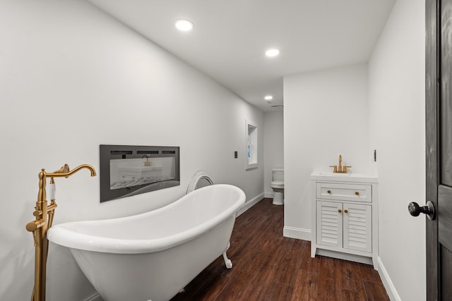 bathroom featuring toilet, recessed lighting, baseboards, wood finished floors, and a soaking tub