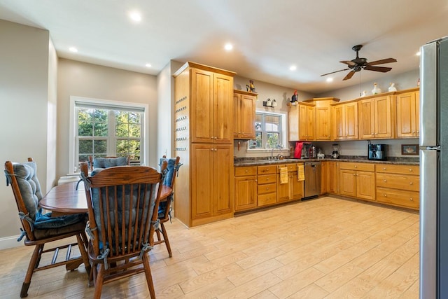 kitchen with ceiling fan, sink, stainless steel appliances, dark stone counters, and light hardwood / wood-style floors