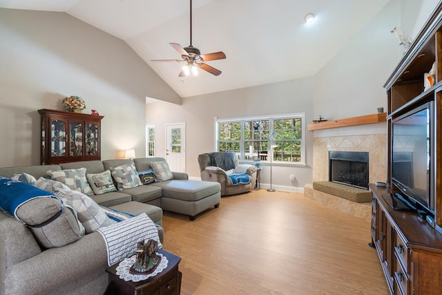 living room with ceiling fan, light wood-type flooring, high vaulted ceiling, and a tiled fireplace