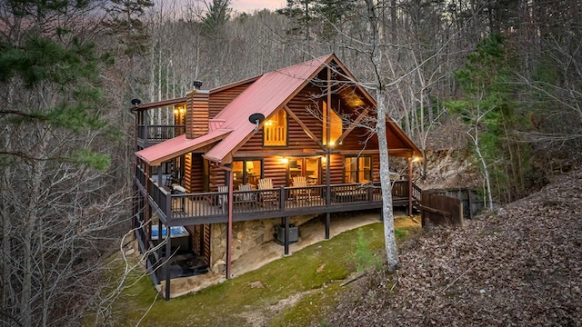 back of property at dusk with central air condition unit, log siding, a chimney, metal roof, and a deck