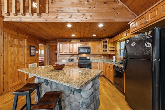 kitchen with light stone countertops, wood walls, wood ceiling, light wood-style floors, and black appliances