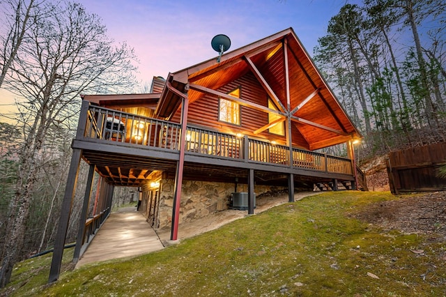 rear view of house with cooling unit, a wooden deck, stone siding, faux log siding, and a lawn