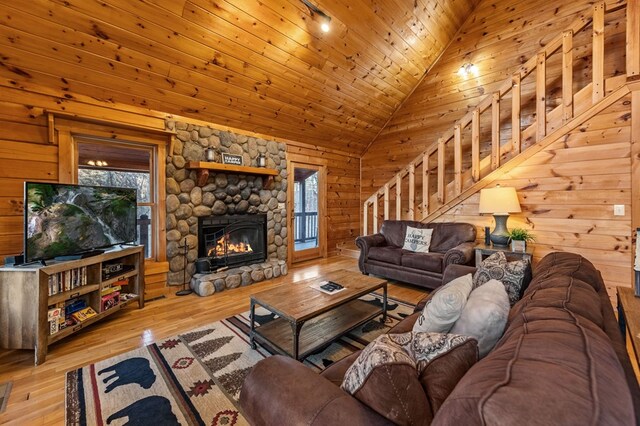 living room with stairs, vaulted ceiling, a stone fireplace, wooden ceiling, and hardwood / wood-style flooring