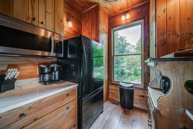 kitchen with wood walls, wood ceiling, light stone counters, light wood-type flooring, and black refrigerator