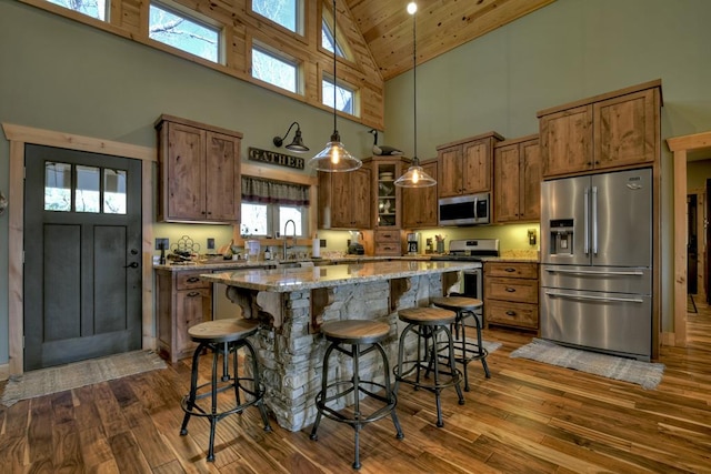 kitchen with appliances with stainless steel finishes, brown cabinetry, hanging light fixtures, and a kitchen bar