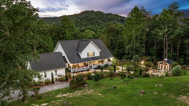 back of property at dusk with metal roof, a porch, a lawn, and a wooded view