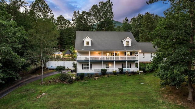 back of property featuring a balcony, covered porch, and a lawn