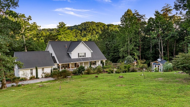 view of front facade with covered porch, a forest view, metal roof, and a front lawn