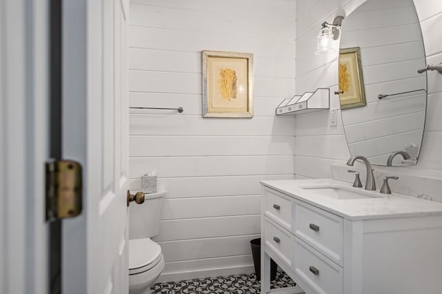 bathroom featuring vanity, toilet, and wooden walls