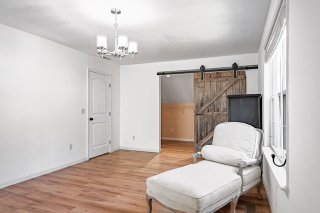 living area featuring light wood-style flooring, a barn door, a textured ceiling, a chandelier, and baseboards