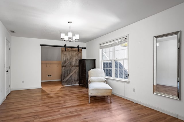 sitting room featuring visible vents, a barn door, wood finished floors, a chandelier, and baseboards