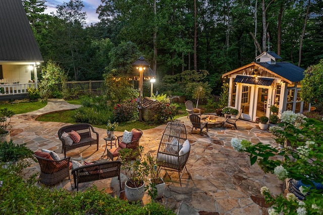 patio terrace at dusk with a storage structure, an outdoor fire pit, fence, and an outbuilding