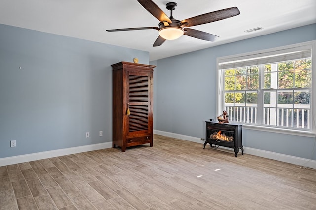 empty room with a wood stove, light wood finished floors, visible vents, and baseboards