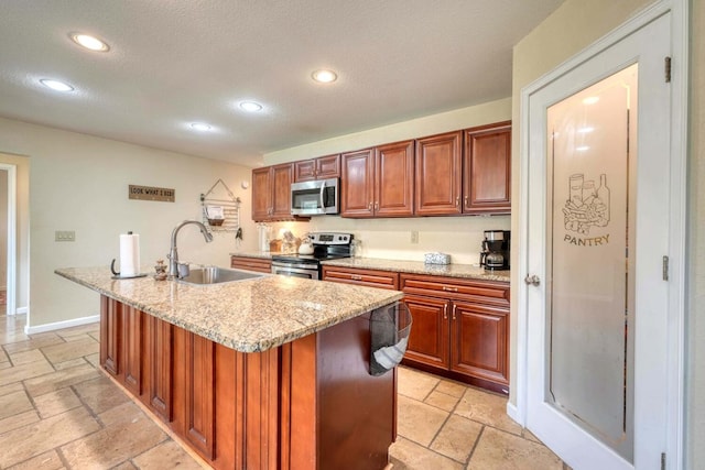 kitchen with light stone countertops, appliances with stainless steel finishes, a textured ceiling, sink, and an island with sink