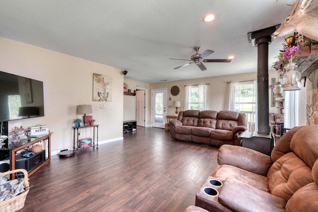 living room with a textured ceiling, a wood stove, ceiling fan, and dark wood-type flooring