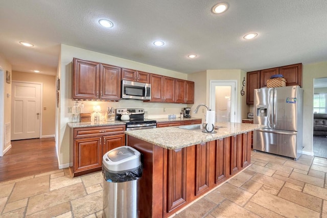 kitchen with a center island with sink, light stone counters, sink, and appliances with stainless steel finishes