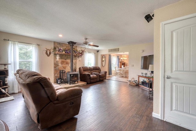 living room featuring a wood stove, ceiling fan, dark wood-type flooring, and a healthy amount of sunlight