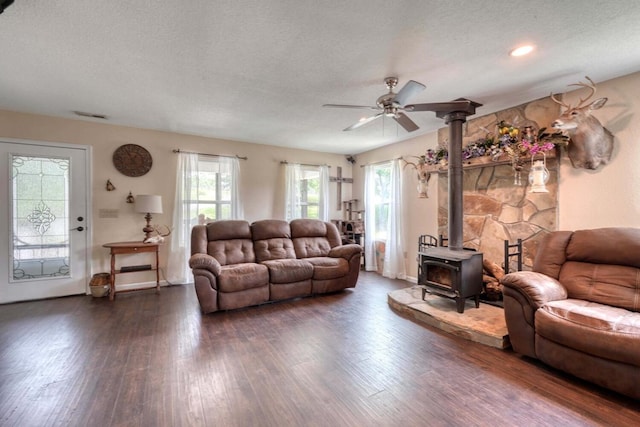 living room featuring a wood stove, ceiling fan, dark hardwood / wood-style floors, and a textured ceiling