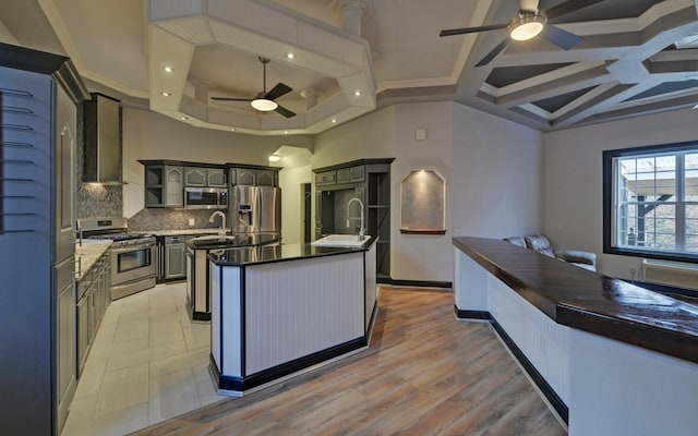 kitchen featuring backsplash, a kitchen island with sink, sink, wall chimney exhaust hood, and appliances with stainless steel finishes