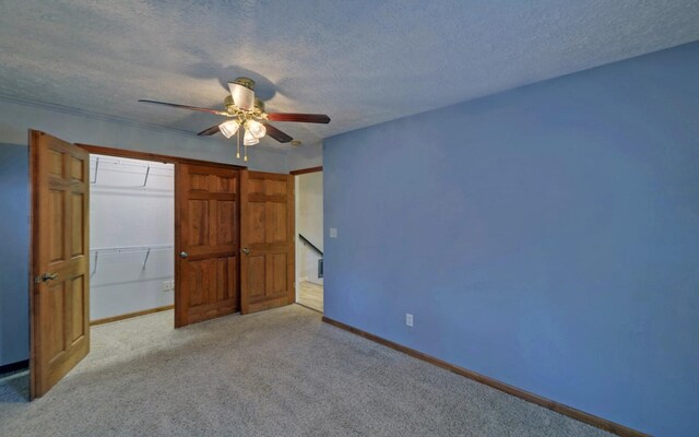 unfurnished bedroom featuring ceiling fan, a closet, light colored carpet, and a textured ceiling