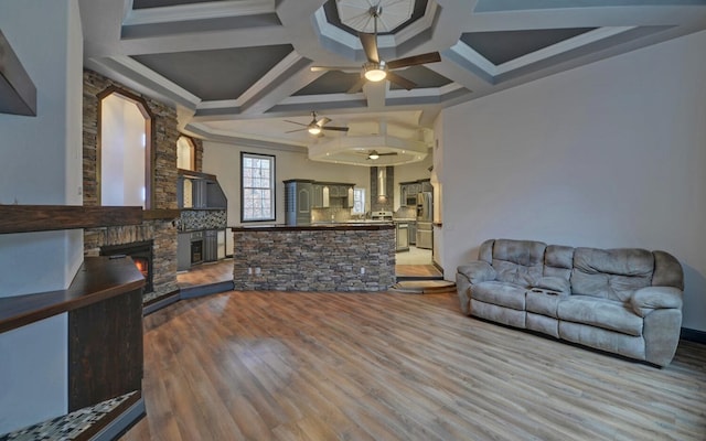 living room featuring coffered ceiling, ceiling fan, crown molding, hardwood / wood-style floors, and a stone fireplace